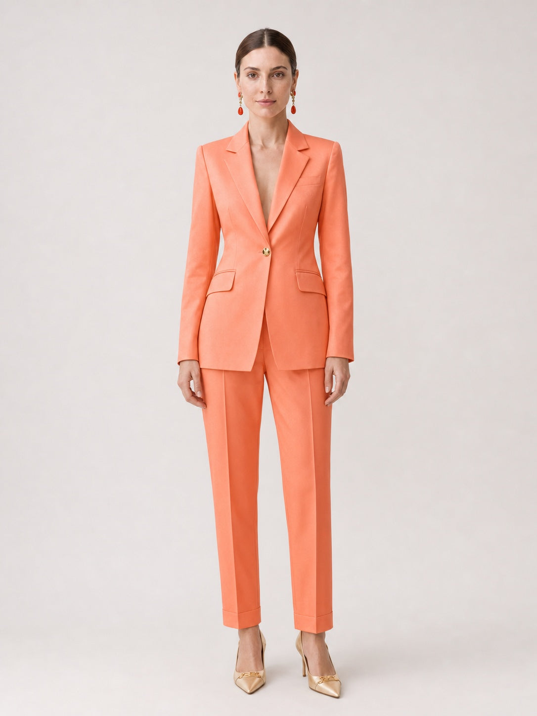 A woman wearing a pikywiky orange tailored single-breasted blazer and slim-fit trousers with a cuffed hem.
