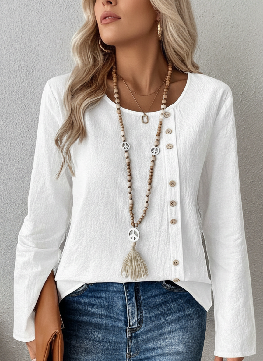 pikywiky white long sleeve blouse with asymmetrical side button detail and round neckline worn with beaded necklace